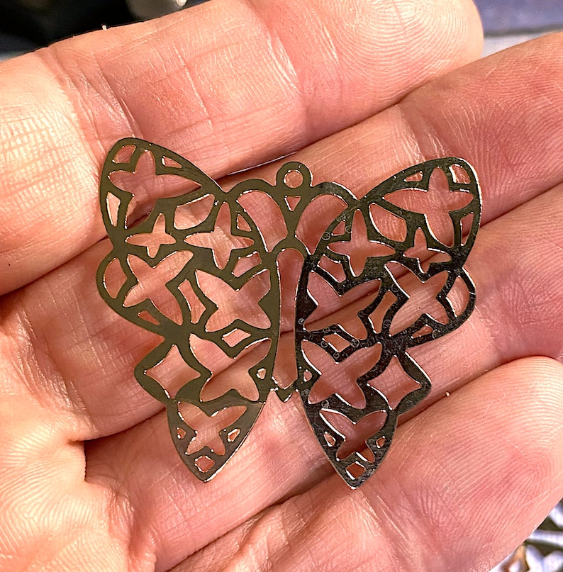 May include: A gold-colored, openwork butterfly pendant with a delicate design. The butterfly's wings feature a pattern of intersecting shapes. The pendant has a small loop at the top for hanging.