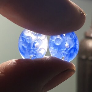 May include: Two blue glass buttons with a white floral design. The buttons are round and have four holes.