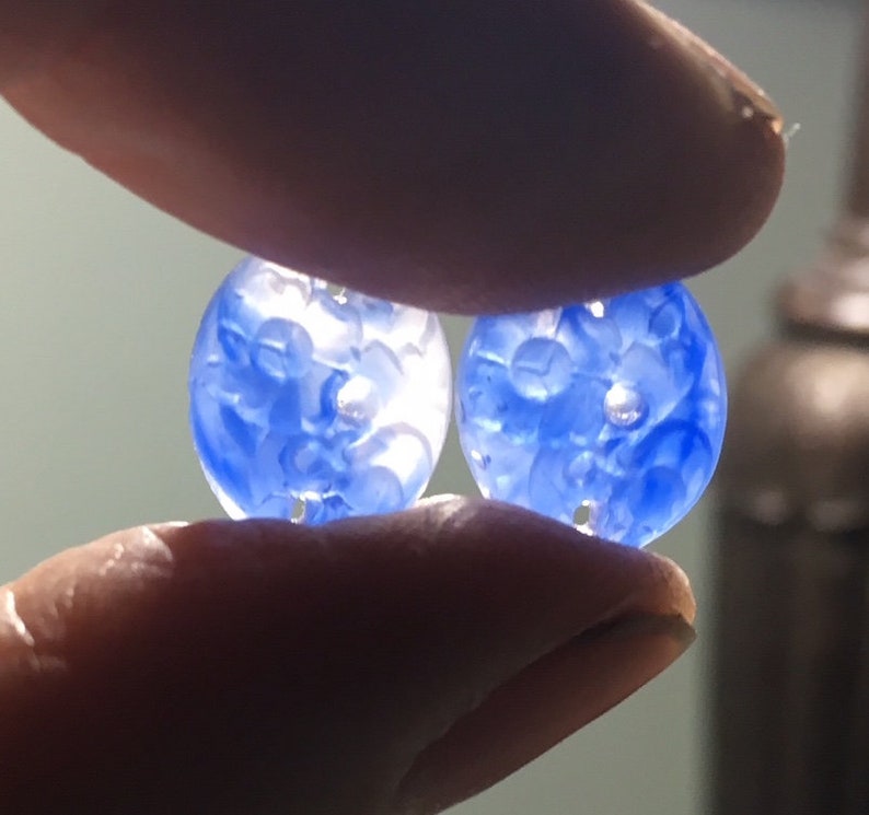 May include: Two blue glass buttons with a white floral design. The buttons are round and have four holes.