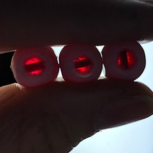 Puede incluir: Tres cuentas redondas blancas con un centro rojo transl&uacute;cido. El centro de cada cuenta tiene una l&iacute;nea horizontal.