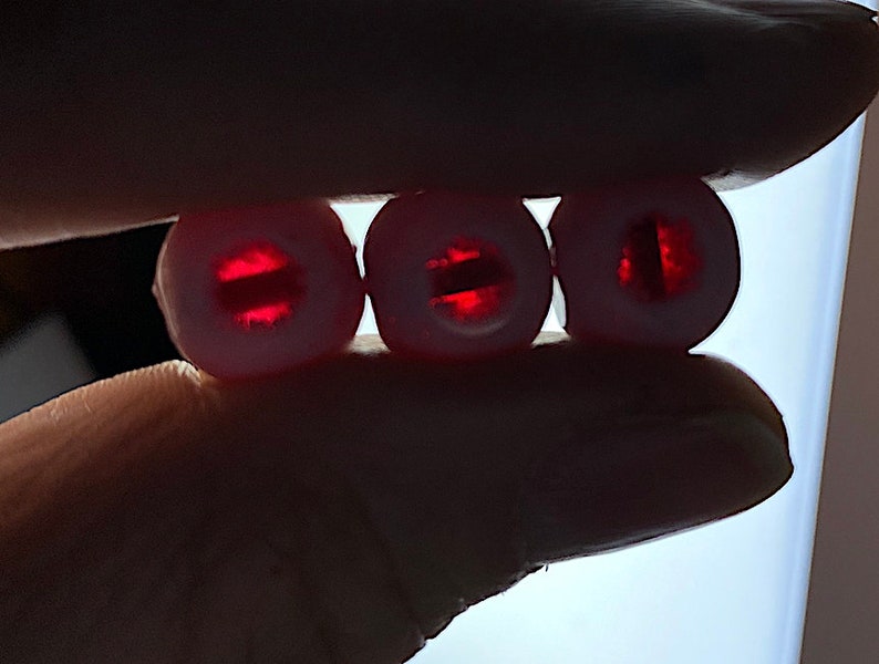 Puede incluir: Tres cuentas redondas blancas con un centro rojo transl&uacute;cido. El centro de cada cuenta tiene una l&iacute;nea horizontal.