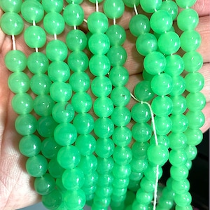 Puede incluir: Una hebra de cuentas redondas de color verde brillante, probablemente de jade o vidrio, enhebradas en un hilo blanco. Las cuentas son lisas y pulidas, con un ligero brillo.