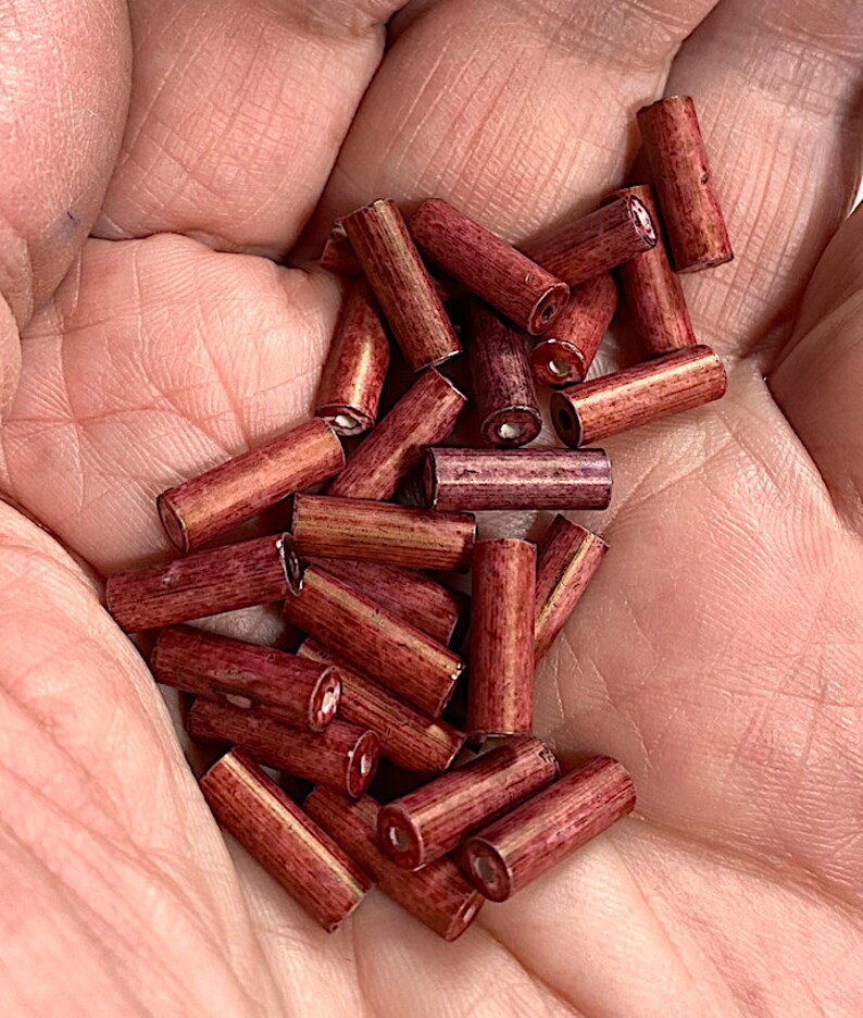 May include: A pile of approximately 20 small, wooden, red-brown beads. The beads are cylindrical in shape and have a slightly textured surface.