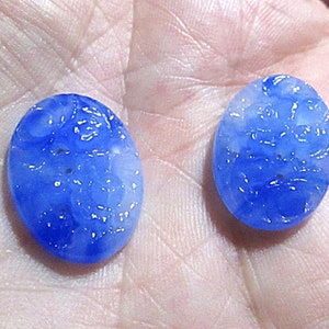 May include: Two oval-shaped blue glass buttons with a white floral design. The buttons have a slightly textured surface.