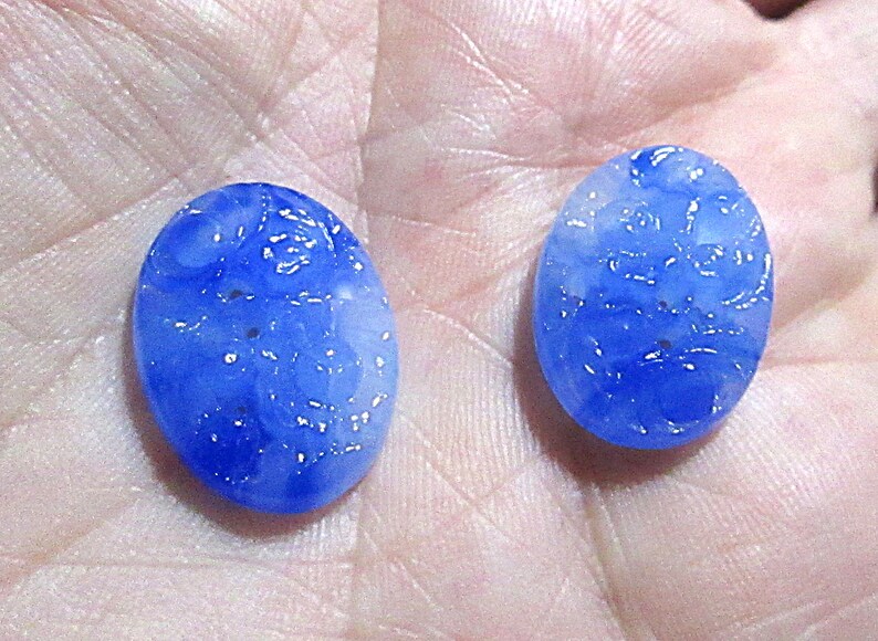 May include: Two oval-shaped blue glass buttons with a white floral design. The buttons have a slightly textured surface.