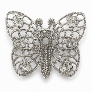 May include: A silver-colored butterfly-shaped brooch with an openwork design. The brooch features intricate details, including floral accents and a textured body. The wings have a delicate, lacy appearance, and the overall design is symmetrical.