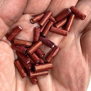 May include: A pile of small, wooden beads in a deep red colour. The beads are cylindrical in shape and have a smooth, polished finish.