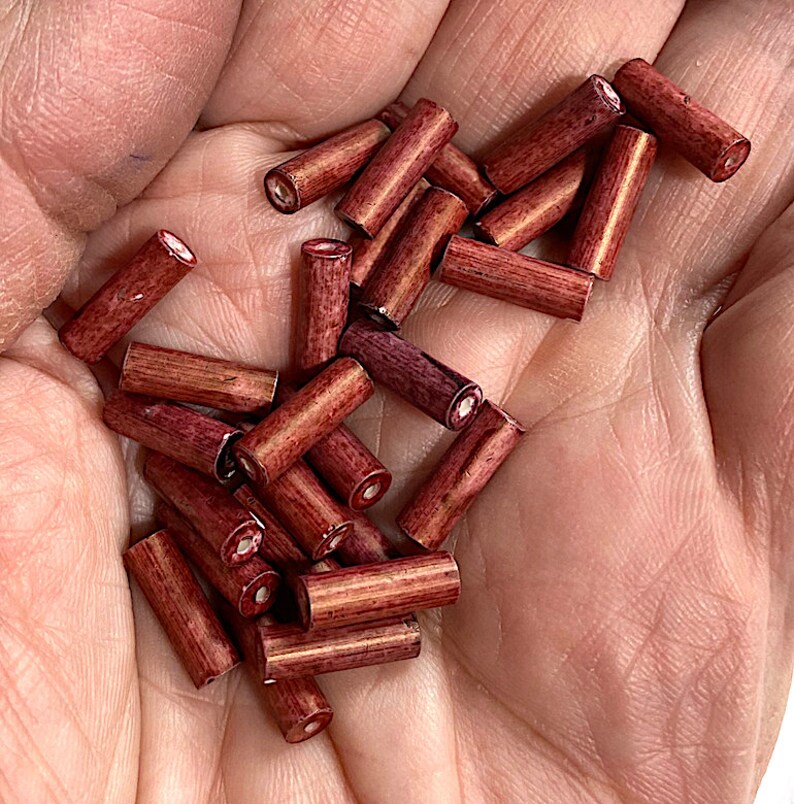 May include: A pile of small, wooden beads in a deep red colour. The beads are cylindrical in shape and have a smooth, polished finish.