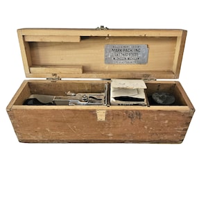 Op de afbeelding: Open houten kist met compartimenten voor gereedschap en benodigdheden. De kist heeft een metalen plaat met tekst. De kist is gemaakt van lichtbruin hout en heeft een scharnierend deksel. De kist is open en toont de inhoud.