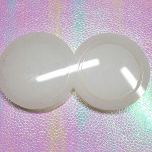May include: Two white round resin moulds with a slightly textured surface. The moulds are joined together and are perfect for creating coasters or other crafts.