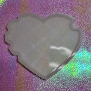 May include: A heart-shaped, glittery, clear resin tray with a scalloped edge. The tray has a grid pattern on the inside. The tray is on a holographic, iridescent surface.