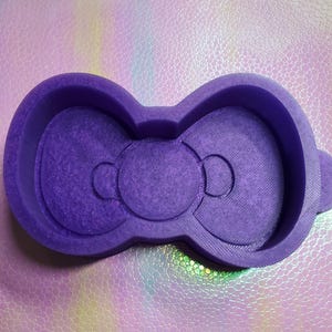 Puede incluir: Molde de silicona morado con forma de lazo con dos círculos en el centro.