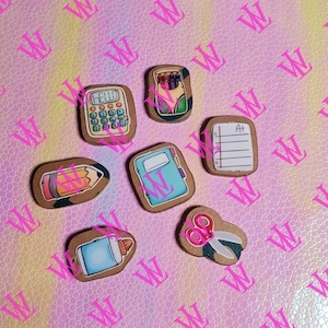 May include: Six wooden cutouts with a school theme. The cutouts are decorated with images of a calculator, a pencil, a notebook, a glue stick, scissors, and a box of crayons.