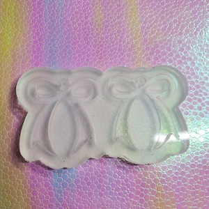 Puede incluir: Un molde de silicona transparente para hacer manualidades de resina. El molde presenta dos formas de campana con lazos en la parte superior.