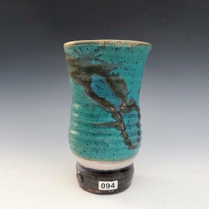 May include: A handmade ceramic tumbler with a turquoise glaze and dark brown accents. The cylindrical body features a textured, ribbed design. The base is dark brown with a white band and the number "094".