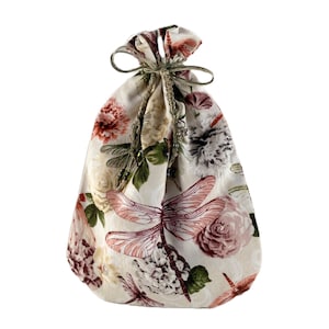 May include: A white fabric drawstring bag with a floral and dragonfly print. The bag is tied with a brown ribbon.