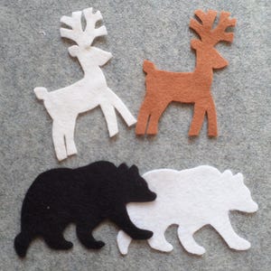 May include: Felt animal cutouts in white, brown, and black. The image features two deer and two bears. The deer are white and brown, and the bears are black and white. The cutouts are on a gray background.