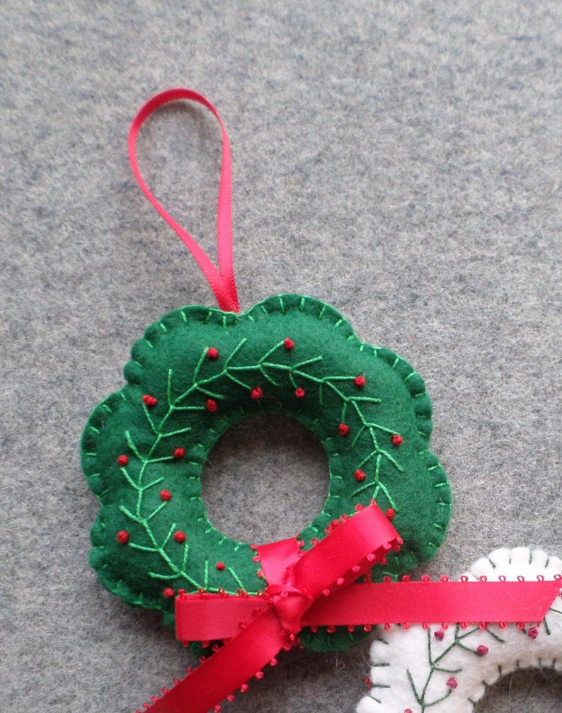 May include: A handmade green felt Christmas wreath ornament with red berry accents and a red satin ribbon bow. The wreath is embroidered with green vines and red berries. A pink ribbon loop is attached for hanging.