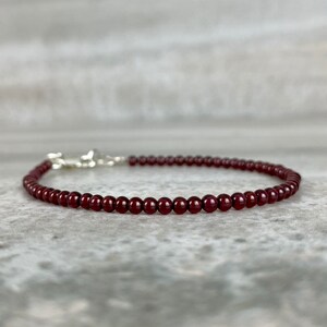 May include: A delicate red gemstone bracelet with a silver clasp. The bracelet is made of small, round beads.