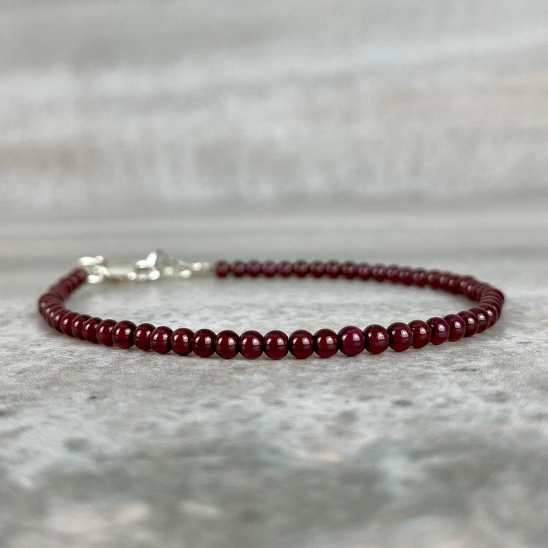 May include: A delicate red gemstone bracelet with a silver clasp. The bracelet is made of small, round beads.