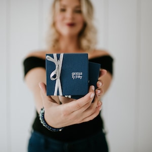May include: A navy blue gift box with a silver ribbon and the text "gems by kiley" on the front.