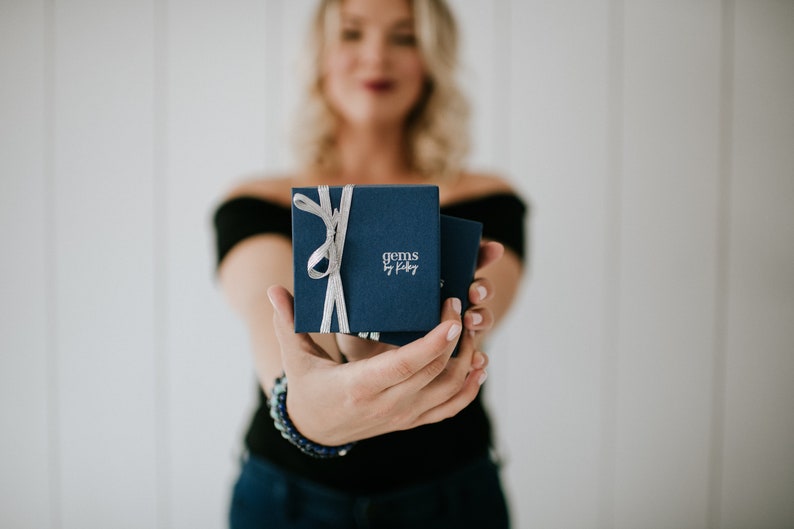 May include: A navy blue gift box with a silver ribbon and the text "gems by kiley" on the front.