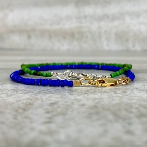 May include: Two beaded bracelets, one blue and one green, with a gold clasp.