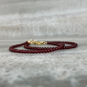 May include: A delicate necklace made of small, dark red garnet beads. The necklace is strung on a gold chain and has a gold clasp.