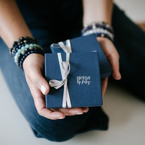 May include: Two navy blue gift boxes with silver ribbon bows. The top box has the text "gems by Kaley" printed on the front.