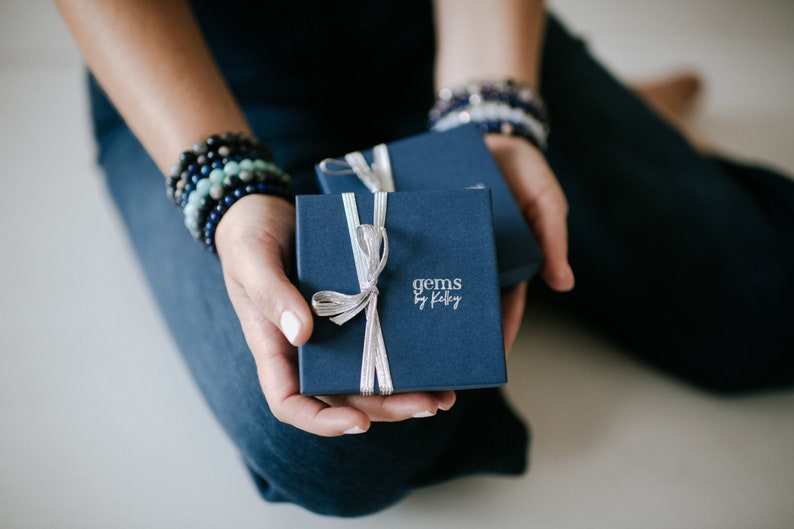 May include: Two navy blue gift boxes with silver ribbon bows. The top box has the text "gems by Kaley" printed on the front.