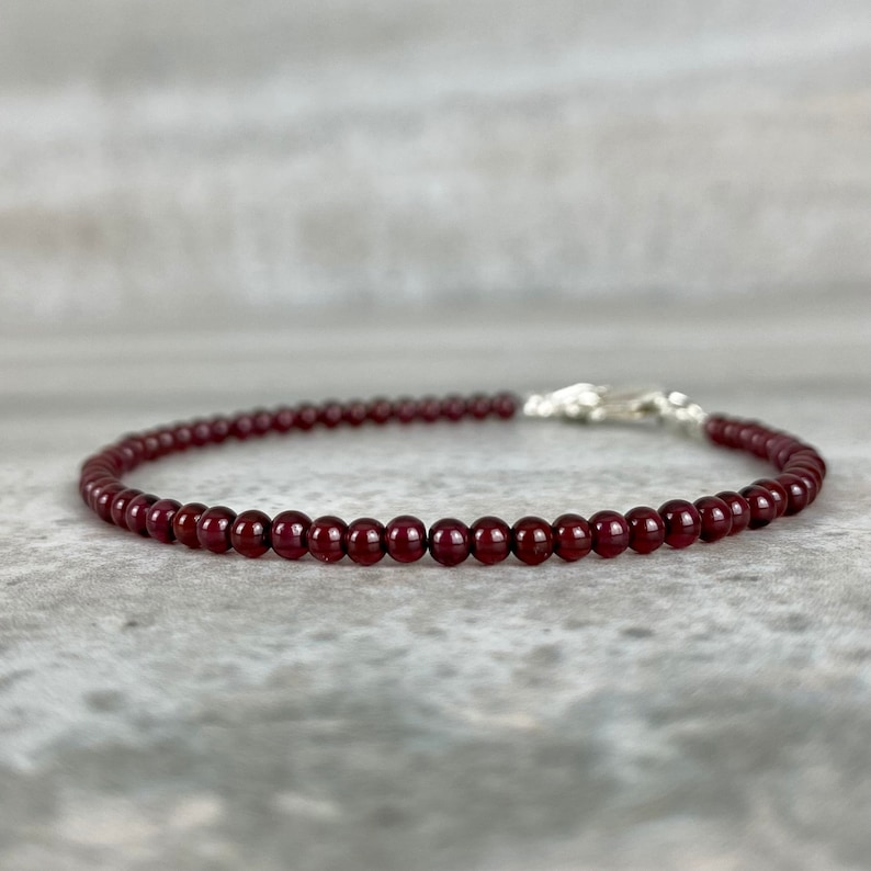 May include: A delicate bracelet made with small, dark red garnet beads and a silver clasp.