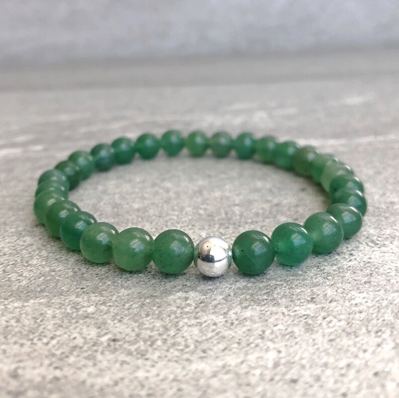 May include: A stretch bracelet composed of smooth, round green aventurine beads. The circular design features a single polished silver-toned metal bead positioned prominently among the green gemstone beads, creating a uniform and simple accessory.