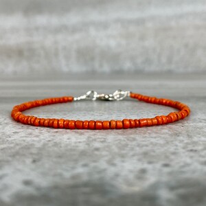 May include: A simple orange beaded bracelet with a silver clasp.