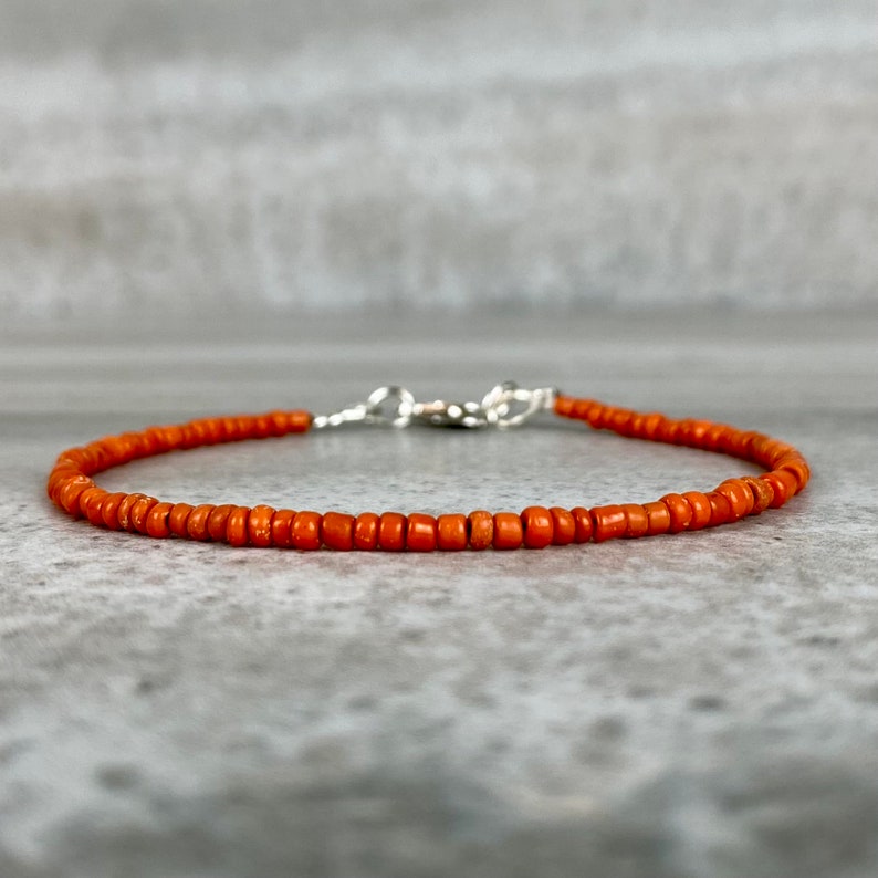 May include: A simple orange beaded bracelet with a silver clasp.
