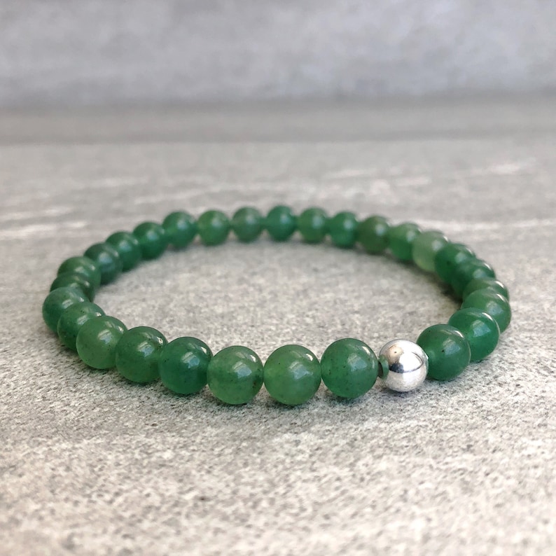 May include: A stretch bracelet composed of smooth, round green aventurine beads. The circular arrangement features a single polished silver-toned metal bead integrated into the strand, creating a consistent pattern of green stones with one metallic accent.