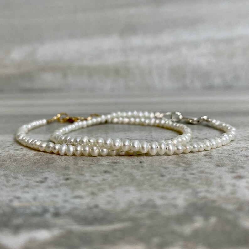 May include: Two delicate pearl necklaces with gold and silver clasps. The necklaces are layered on a gray surface.