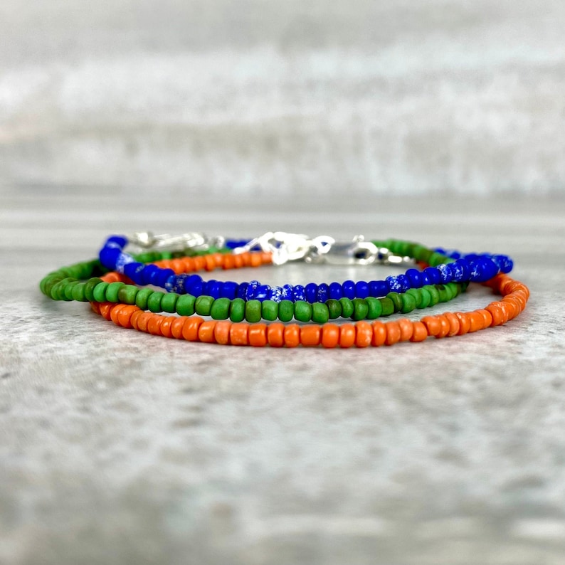May include: Three layered bracelets with orange, green, and blue beads. The bracelets are made of small, round beads and are strung on a silver chain.