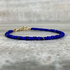 May include: A delicate blue beaded bracelet with a gold clasp. The bracelet is made of small, round beads that are strung together to create a simple and elegant design.