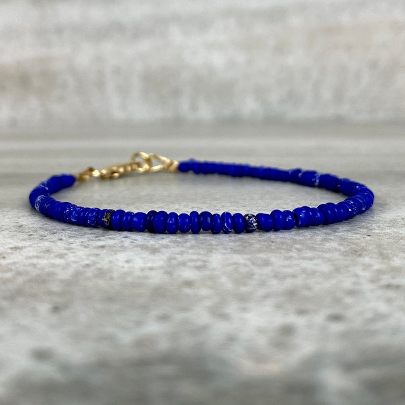 May include: A delicate blue beaded bracelet with a gold clasp. The bracelet is made of small, round beads that are strung together to create a simple and elegant design.