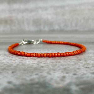 May include: A simple orange beaded bracelet with a silver clasp.