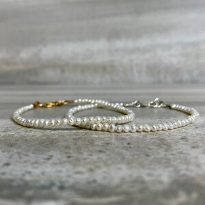 May include: Two delicate pearl necklaces with gold and silver clasps. The necklaces are layered on a gray surface.