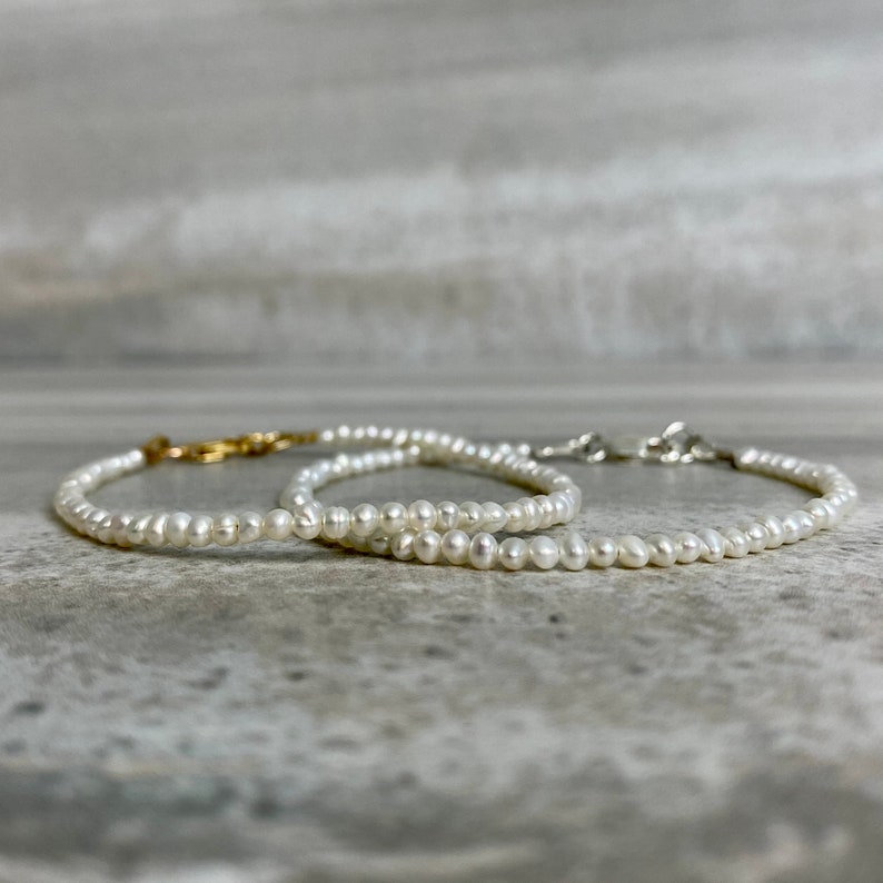 May include: Two delicate pearl necklaces with gold and silver clasps. The necklaces are layered on a gray surface.