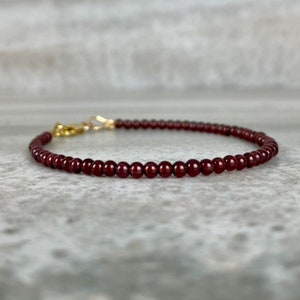 May include: A delicate bracelet made with small, dark red garnet beads and a gold clasp.