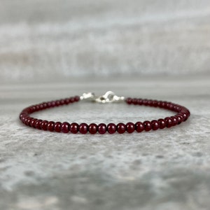 May include: A delicate bracelet made with small, dark red garnet beads. The bracelet is strung on a silver chain with a lobster clasp.