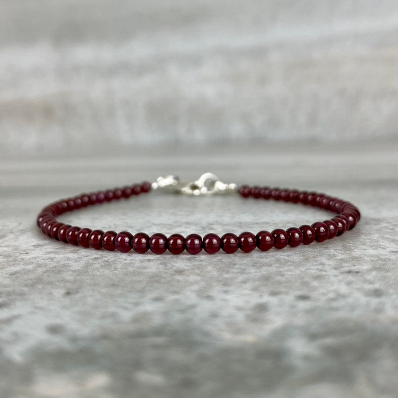 May include: A delicate bracelet made with small, dark red garnet beads. The bracelet is strung on a silver chain with a lobster clasp.