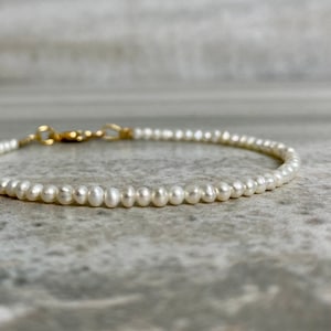 May include: A delicate pearl bracelet with a gold clasp. The bracelet is made of small, white pearls and is perfect for everyday wear.