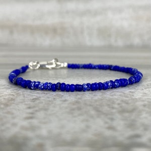 May include: A dainty blue bracelet crafted from small glass beads. The beads feature a speckled white pattern, adding a subtle textural element.