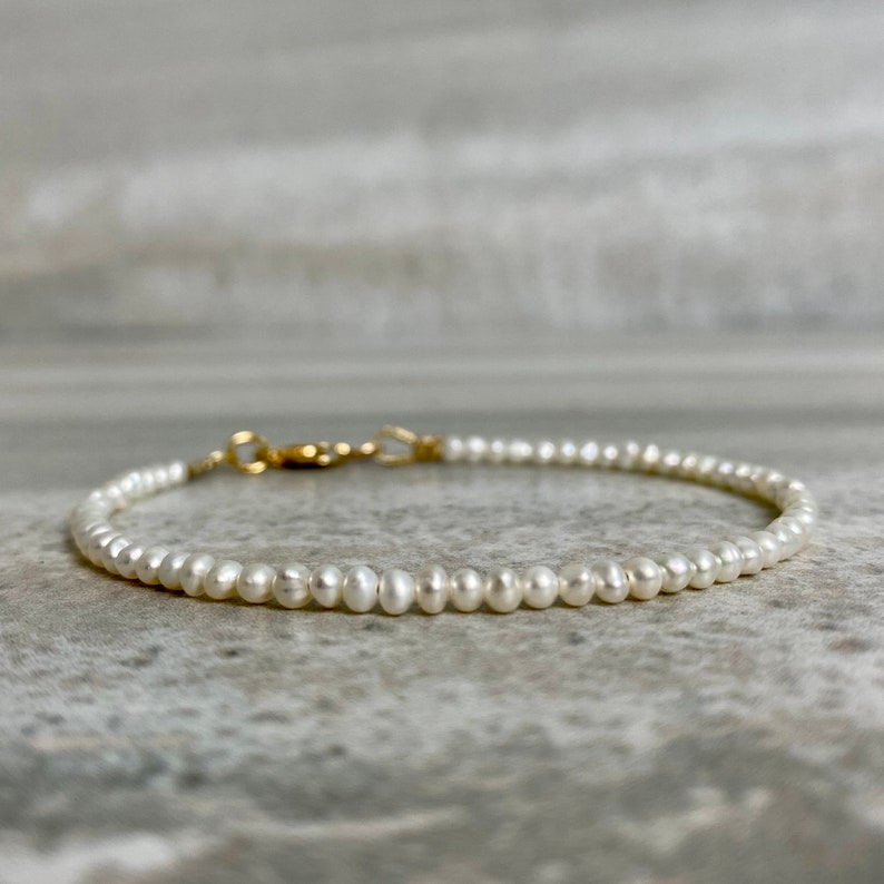 May include: A delicate pearl bracelet with a gold clasp. The bracelet is made of small, white pearls and is strung on a thin gold chain.