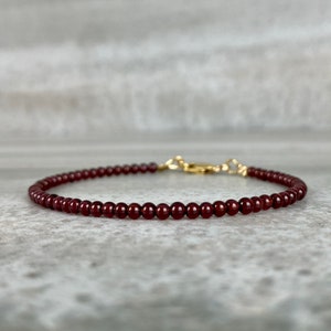 May include: A delicate bracelet made with small, dark red garnet beads and a gold clasp.