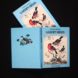 May include: Two blue hardback books with the title "Garden Birds" and illustrations of birds on the covers. The book on the left is closed and the book on the right is open to a page with a red robin and other birds on a branch.